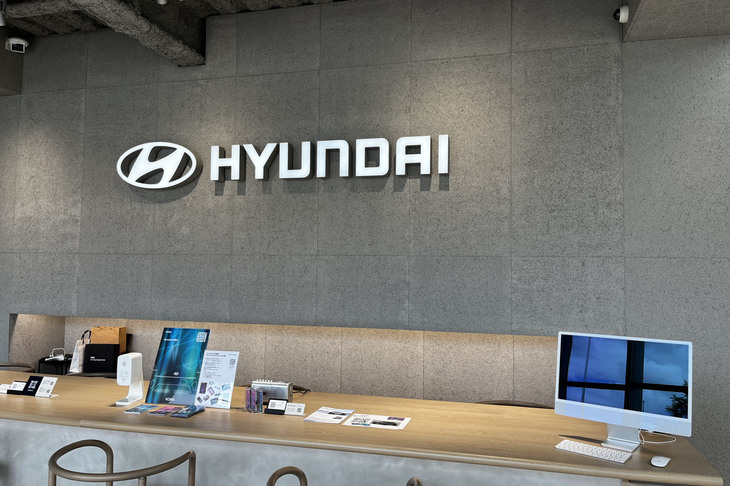 「ヒョンデカスタマーエクスペリエンスセンター横浜」の受付カウンター。グレーで統一された壁には、木毛セメント板などの再生可能素材が使用されている。各種サービスを行うだけではなく、ヒョンデが目指すクリーンモビリティーやサステイナブルという世界観を伝える役割も担うという。