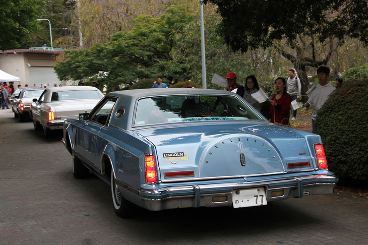 連なって会場を後にするフルサイズのアメリカ車。最後尾は1977年「リンカーン・コンチネンタル マークV」。ダウンサイズされる直前、巨大な体軀（たいく）を誇った最後の世代のコンチネンタル。