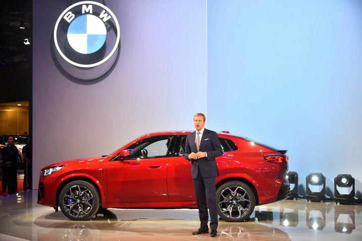 BMWのブースでプレスカンファレンスに臨むBMW会長のオリバー・ツィプセ氏と、新型車「BMW iX2」。
