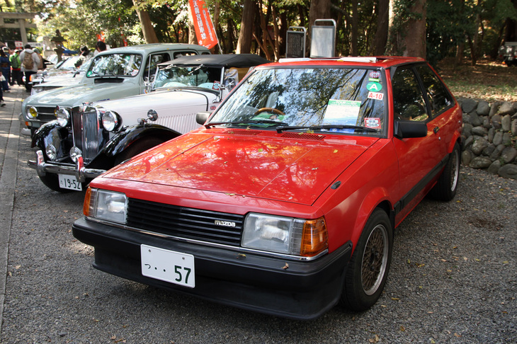 1982年「マツダ・ファミリア1500XG」。販売台数に対する残存率の低さではトップクラスであろう“赤いファミリア”の、電動スライディングルーフを標準装備した初期の最上級グレード。アルミホイール、エアダムスカートにドアミラーはノンオリジナルだが、そうした改造も“当時風”である。