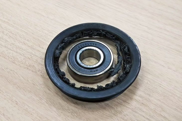 壊れたテンションプーリーのどアップ。ご覧の通り、残っているのは軸受けと縁の部分だけで、残りはすっかり砕け散っている。有識者いわく「ベアリングが固着しちゃったんじゃないの？」とのことだが……。