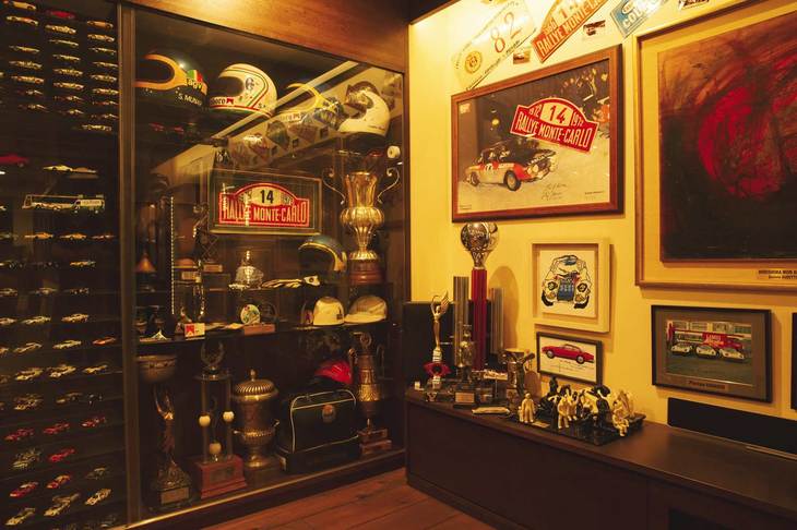 2階のコレクションルームに展示されているムナーリをはじめとするラリードライバーのヘルメットや彼らが手にしたトロフィーなどの記念品の数々。左に見えるのは1/43スケールのミニチュアカーのケース。ミニチュアカーはものすごい台数で、かなりの数を原田さんがキットを組んだもの。もう増やせないらしい。