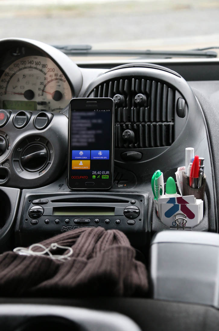 フラヴィオさんの“仕事場”。領収書に記入するペン、呼び出し電話番号が書かれたカード、防寒用の帽子、そしてタクシーメーターの機能を補完するスマートフォンも。