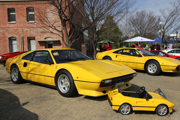 1981年「フェラーリ308GTBエボルツィオーネ」。カタログモデルではないが、オーナーいわくメーカー製のスペシャルという個体。ノーマルと違い、大きなエアダムスカートが付いたボディーの鋼板が薄く車重はFRPボディーの初期型308GTBより軽量で、ホイールが標準の14インチともオプションの16インチとも異なる15インチになっている。エンジンはハイリフトカムやハイコンプピストンが入っていて、高回転域の回りかたが違うとのこと。前に置かれた子供用の308は、「フェラーリF12」の電動カーをベースにオーナー自ら改造したスペシャル。