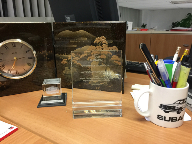 卓上には、スバル・イタリアから授けられた盾やノベルティーが。マグカップに描かれた2代目の“丸目仕様”「レオーネ」が懐かしい。