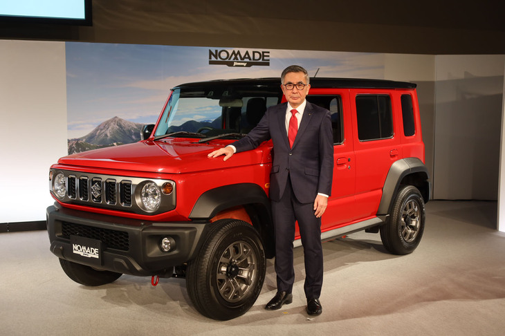 スズキの新型車「ジムニー ノマド」と、フォトセッションに臨む鈴木俊宏 代表取締役社長。“5ドアのジムニー”の国内導入が遅れたことについて鈴木社長は、「『ジムニー／ジムニー シエラ』の納車待ちが解消できていない状況で、自分自身はジムニー ノマドの追加的な販売に反対していたものの、営業サイドの（ジムニー ノマドを導入しユーザーへの配車切り替えを実施するなどしてデリバリーの問題を改善できるという）意見も検討しつつ議論を重ね、この時期になりました」と説明した。