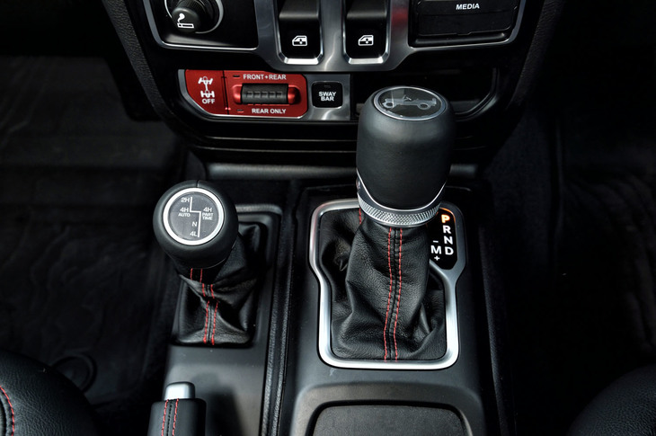 「ラングラー ルビコン」のシフトレバー（右）と駆動切り替えレバー（左）。写真奥の赤いパネル内に、前後ディファレンシャルをロックする「トゥルロック」スイッチが配置される。これを押すだけで前後または後ろのみをロックでき、前後ロック時にはトルクを4輪に均等分配する。