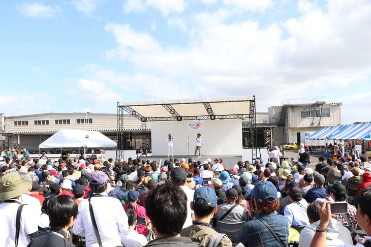 メインステージで10時から行われた開会式には、多くのファンが参加。用意された席だけでは足りず、立ち見が出るほどだった。ステージの後方には、参加者の休憩場所として巨大なテントが設置されており、そちらから開会式を見守る人も多かった。