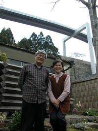 峰尾章子さんの自宅の前で、峰尾さん（右）と高尾山の自然を守る市民の会の事務局長、橋本良仁さん。背後には無機質な橋がつくられている。