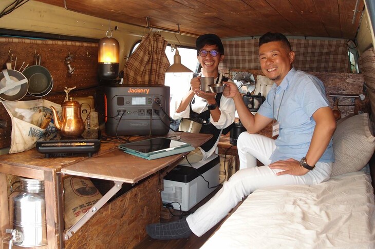 Jackeryが活躍するシチュエーションを最後にもうひとつ。オールドタイマーな「マツダ・ボンゴ」を“リノベ”して、こんなにも気持ちの安らぐ空間をつくってしまったバンキャンプコーディネーターのヘンミマオさん（写真奥）、その車内でも「1000 Pro」は大活躍する。バーナーに頼らずとも瞬時にお湯を沸かし、おいしいコーヒーを入れることができた。センスよくウッディに仕立てられた車内はたまらなく快適で、できればこのまま自宅まで送ってほしいくらいである……もちろんJRで帰りましたが！
