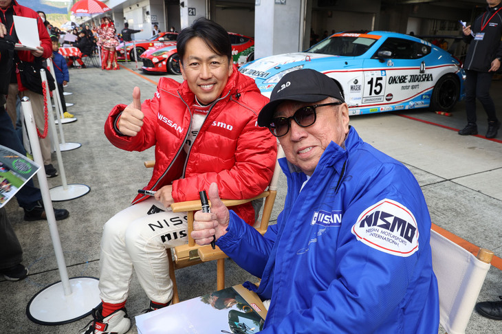 サインする手をちょっと止めてカメラ目線をくれたのは、“Zの柳田”こと柳田春人氏、2011-12年のSUPER GT GT500クラスを連覇した柳田真孝氏の柳田父子。
