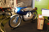 「RM62」。1962年、世界一過酷なレースと言われていたマン島TTレースの50ccクラスで世界GP初優勝を飾り、その年のライダー、メーカー両タイトルを獲得した記念すべきマシン。50ccの空冷2ストローク単気筒、最高出力は9.0ps。右のスーツケースは、当時遠征メンバーが買い揃えて使用していたもの。