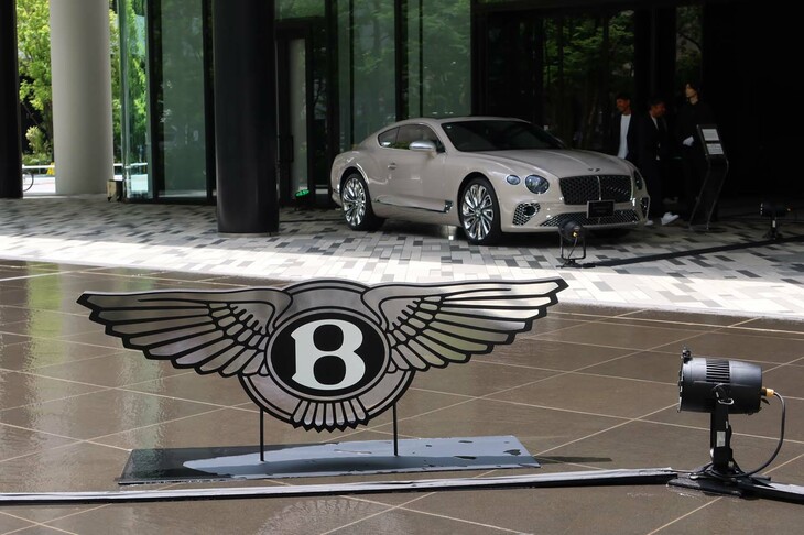 第4世代にあたる新型「ベントレー・コンチネンタルGT」の発表会場に飾られた、ベントレーのエンブレム。写真奥は、現行型（第3世代）の「コンチネンタルGTマリナー」。