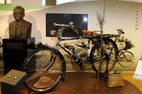 スズキの自動車業界における処女作であるバイクモーター「パワーフリーE2」（1952年）。36ccの空冷2ストローク単気筒、最高出力1.0ps/4000rpm。左の胸像は2代目社長の鈴木俊三。