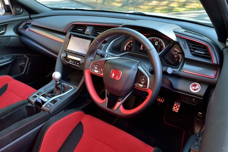 スポーティーさが際立つ室内。下端を水平にカットした「D」シェイプのステアリングが装着されるほか、インパネにはアルマイト調の赤ストライプをあしらったカーボン調パネルが張られる。