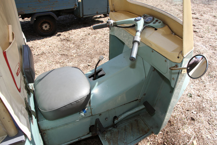 「ダイハツ・ミゼットDKA」の運転席。バーハンドルでアクセルは右グリップ、右前方のペダルはブレーキ、右後方に見えるのはエンジン始動用キックペダル。クラッチペダルは左前方にあり、ギアボックスは3段MT。