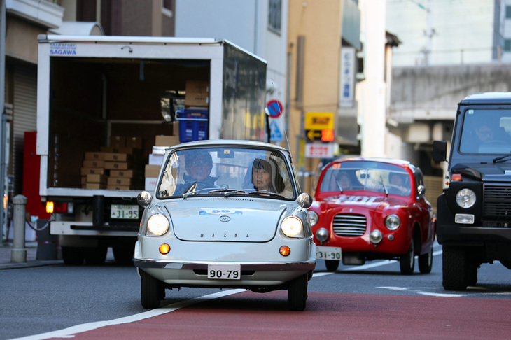 汐留イタリア街の周辺道路を、駐停車車両を縫うように走る1961年「マツダR360クーペ」。続くのは1948年「フィアット500Bザガート パノラミカ」。