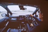四輪制御技術のテストカーの運転シーン（写真はスライド資料）。インストゥルメントパネル中央には、駆動力の前後配分や横Gの変化を示すモニターが装着されている。