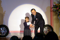 鈴木愛渚ちゃんは4歳。おばあちゃんの干し柿を題材にしての受賞だ。右は、ブリヂストン社長の荒川詔四氏。