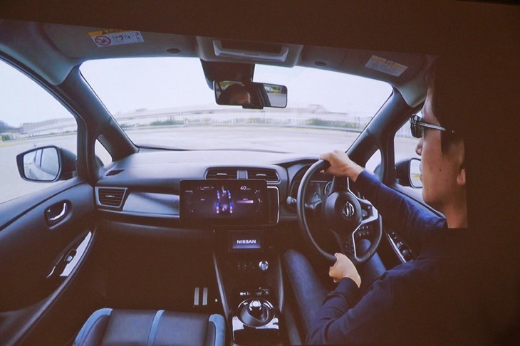 四輪制御技術のテストカーの運転シーン（写真はスライド資料）。インストゥルメントパネル中央には、駆動力の前後配分や横Gの変化を示すモニターが装着されている。