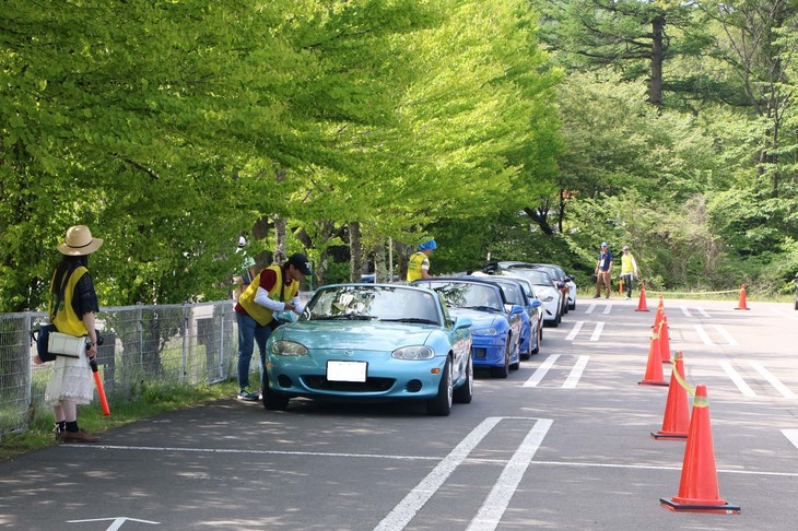 朝8時のゲートオープンとともに、会場に続々と入場してくる「ロードスター」。その1000台以上を駐車スペースに誘導する会場スタッフも、ロードスターオーナーのボランティアたちだ。これだけの規模ながら、運営はすべてロードスターを愛する者同士の協力で成り立っていることに、ファンの結束力を感じさせる。