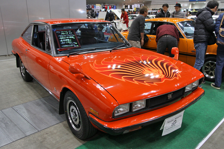 1979年「いすゞ117クーペXC-J」。俗に量産角目と呼ばれる後期117クーペの、2リッターエンジンを積んだスターシリーズのモデル。「ポンティアック・ファイアーバード」のようなボンネットのデカールをいぶかしむ向きもあるだろうが、これが本来の姿（メーカー純正）なのだ。いすゞスポーツの出展で、価格応談。