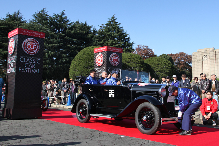 前回までパレードのスタート順は最初に戦前車、以後は生産国別に続いてラストがトヨタ車だったが、今回は生産国を問わず年式順となった。先頭は千葉工業大学 体育会自動車部の1931年「フォードA型フェートン」。右ハンドルだから、おそらく横浜にあった日本フォードの工場で作られたものだろう。レッドカーペット上でいったんエンジンを止めてからクランク始動を試み、見事一発で掛けてスタートした。