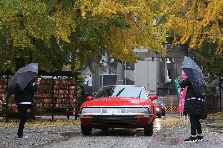 境内では雨のなかを待機していた女性スタッフが到着した車両をスマホで撮影。1975年「シトロエンSM」。