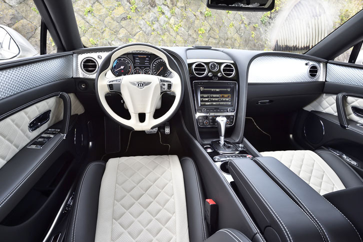 「フライングスパーV8 S」のインテリア。ピアノブラックのウッドパネルとスポーツステアリングホイールが標準で備わるほか、シフトセレクターとシフトパドルにはローレット（ギザギザ）加工が施されている。