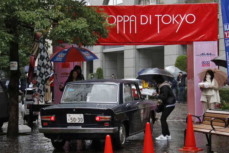 スタートと同様、ゲートをくぐってゴールする1964年「ランチア・フルヴィア2Cベルリーナ」。スタッフがランチを渡している。