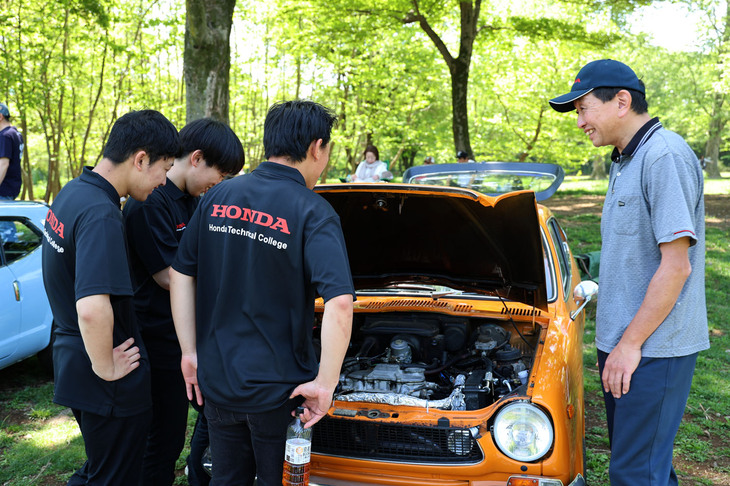 電動コンプレッサー駆動のエアコンを装着した「Z600」のエンジンルームを興味深げに観察する、スタッフを務めたホンダテクニカルカレッジ関東（埼玉県ふじみ野市にあるホンダ系列の自動車専門学校）の学生たち。「S800」や「N360」などのレストアを実践している若い世代との交流にオーナー（写真右端）もうれしそう。