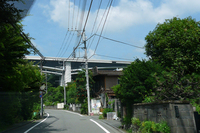 高尾山ICを下りて裏高尾町へ。民家の頭上に圏央道が見える。写真の右側（北側）に八王子JCTがあり、左側が高尾山。
    