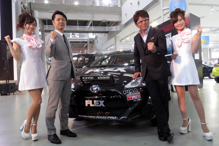 レースクイーンとともに撮影に応じる、俳優の哀川 翔さん（右）と、フレックスの藤崎孝行社長（左）。