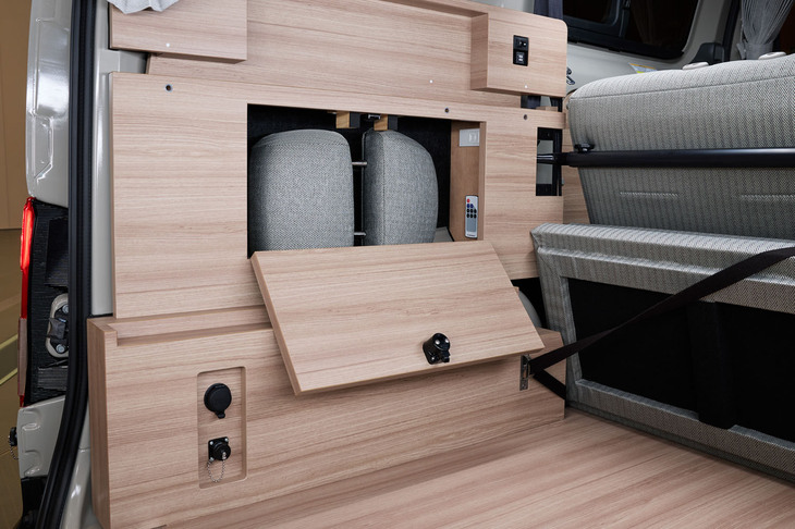 「NV200バネットMYROOM」の車内後方側面には、収納スペースのほか、車外からの給電コネクターや、コンセント、照明・空調のスイッチなどが備わる。写真は「2 in 1シート」のヘッドレストをおさめた状態。