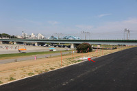 上面のサイクリングロードから見た新堤防。赤い矢印部分に移設された観客席および記念プレートがある。