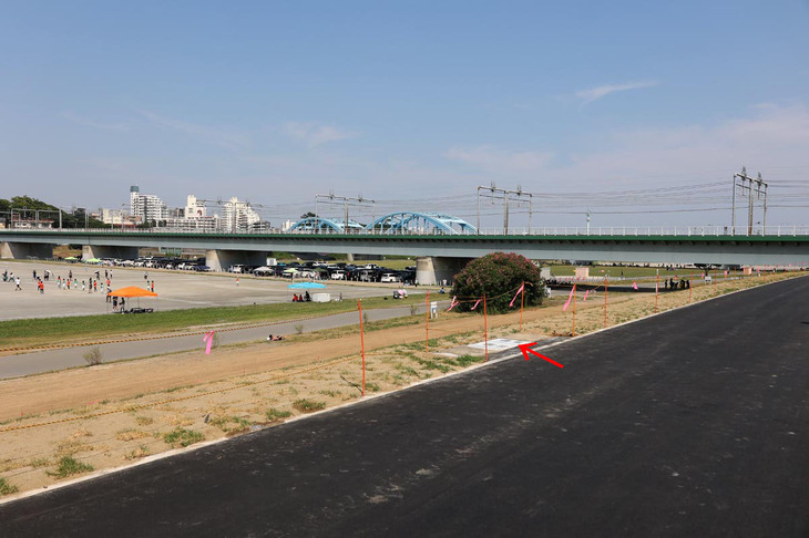 上面のサイクリングロードから見た新堤防。赤い矢印部分に移設された観客席および記念プレートがある。