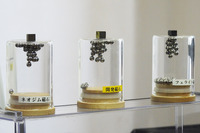 ネオジムやジスプロシウムなどのレアアースを使わない「サマリウム鉄系磁石」（写真中央）の展示。引き寄せられている金属球の数からもわかるとおり、既存のネオジム磁石に迫る磁力を実現している。今後は磁石のスケールアップや、磁束密度、保磁性（耐熱性）が課題となる。