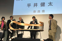 サポートメンバーの川又俊明さん（右）から「注目の匠」に選ばれたのは奈良県代表の木工作家、平井健太さん（右から2番目）。杉材を使った曲木の技術が高く評価された。