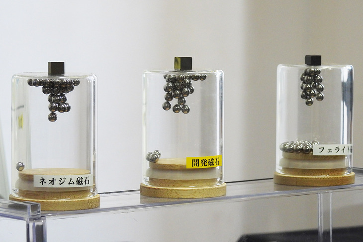ネオジムやジスプロシウムなどのレアアースを使わない「サマリウム鉄系磁石」（写真中央）の展示。引き寄せられている金属球の数からもわかるとおり、既存のネオジム磁石に迫る磁力を実現している。今後は磁石のスケールアップや、磁束密度、保磁性（耐熱性）が課題となる。