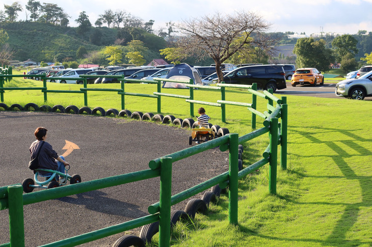 クルマ型の自転車にも乗れる「おもしろ自転車」のコーナー。写真右奥には、乗員を待つ「メガーヌR.S.ウルティム」が見える。