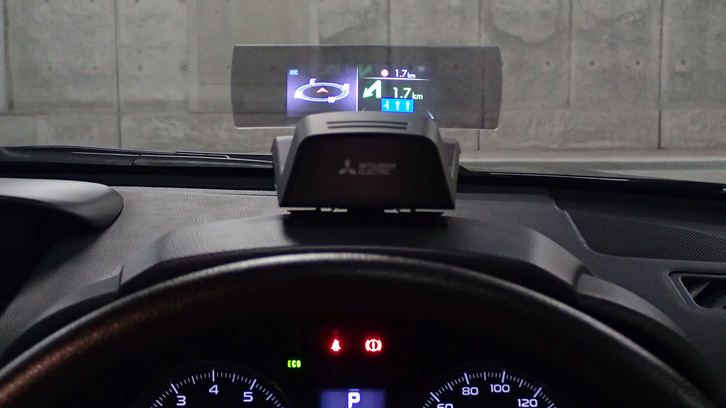 ヘッドアップディスプレイは、メーターナセルの上に乗せることでナビの案内情報を簡略化して表示する。ETC2.0車載機をナビに接続すれば赤信号の残時間表示も、ナビに目を移すことなく得ることができる。（オープン価格）