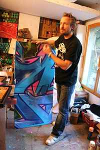 「スプレーペイントは、自らの動きを最も表現しやすいツール」と語る作者。後方には、無数のスプレー缶が。（2014年2月撮影）