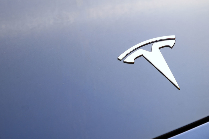 サッシャさんの愛車「テスラ・モデル3」のノーズに輝くエンブレム。「Teala」の頭文字とモーターの断面をモチーフにデザインされているという。モデル3は、2008年の「ロードスター」、2012年の「モデルS」、そして2015年の「モデルX」に続くテスラ第4のモデルとして2016年に登場した。