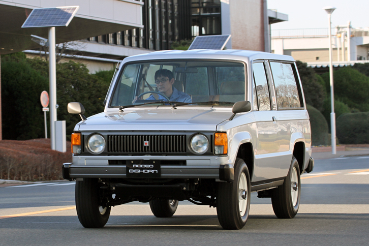 1982年「ロデオ ビッグホーン」。1979年に小型ボンネットトラックの「ファスター」に加えられた4WD仕様が「ファスター ロデオ」。そのシャシーを流用して生まれたSUVの先駆けとなるモデルが、1981年に誕生した初代ビッグホーンである。ロデオ ビッグホーンと名乗っていたデビュー当初は、長短2種のホイールベースがあり、双方にソフトトップ、メタルトップ（バン）を用意。いずれも2ドアで、4ナンバーの商用登録だった。エンジンは2リッターガソリンまたは2.2リッターディーゼル。これはロングのバンで、角張ったスタイリングは初代「レンジローバー」をほうふつさせる。