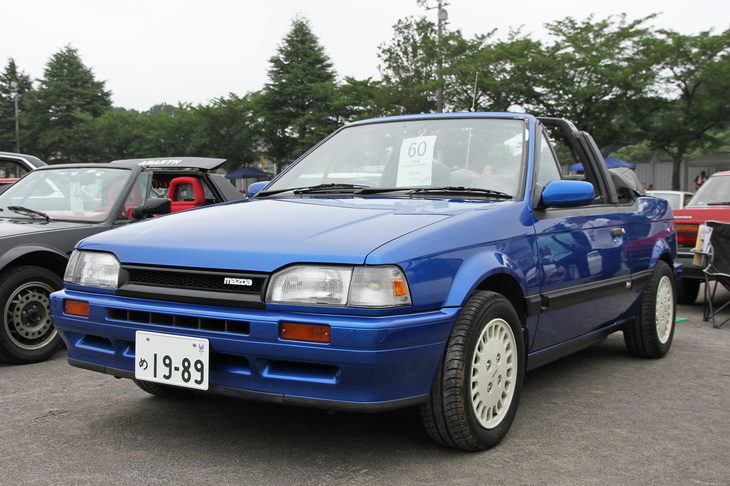 1989年「マツダ・ファミリア カブリオレ」。6代目ファミリアに存在した、歴代唯一となるカブリオレ。1986年に追加設定され、当初は1.5リッターSOHCターボを、この後期型では自然吸気の1.6リッターDOHC 16バルブエンジンを搭載していた。ボディーは「スバル・インプレッサ」用のWRブルーでリペイントされている。