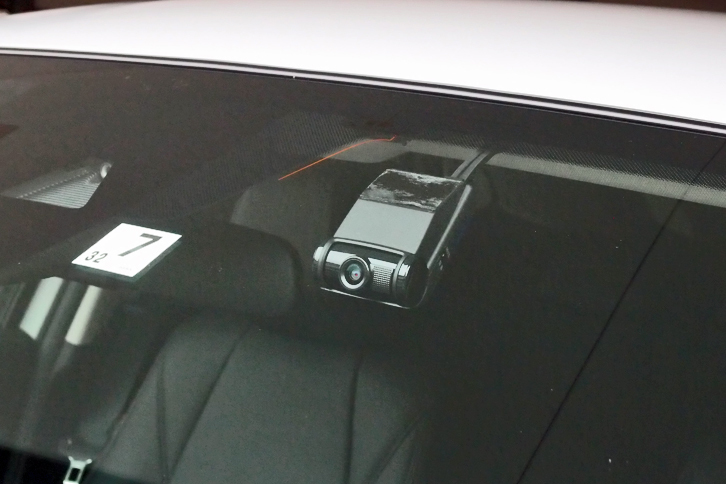 ドライブレコーダーの一例。フロントウィンドウの内側に装着されたカメラ（写真中央）が、車体前方の光景を記録する。