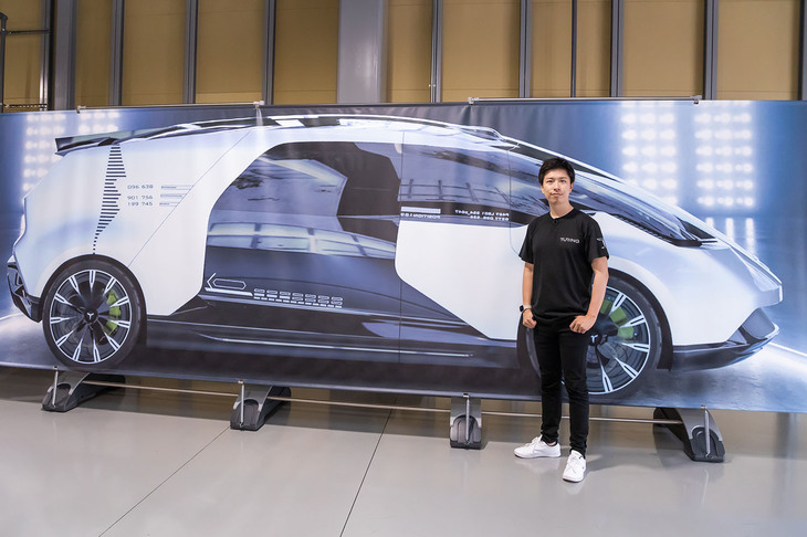 完全自動運転のEVメーカーを目指す日本のスタートアップ企業、Turing（チューリング）の山本一成CEO。背後の画像はAIをフル活用して短期間でつくった同社初のコンセンプトカーだ。