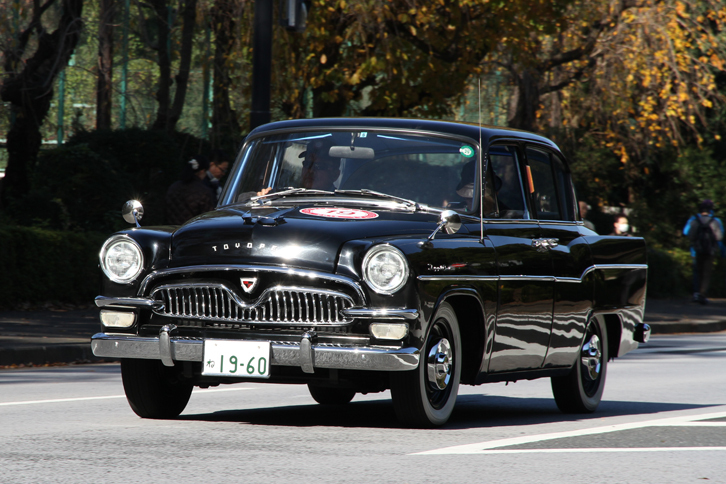 絵画館前を出て、神宮外苑の外周路をいちょう並木に向かう1960年「トヨペット・クラウン」。初代クラウンの最初のマイナーチェンジ以降の、珍しいスタンダード仕様（RS20型）。1.5リッター直4エンジンを搭載。