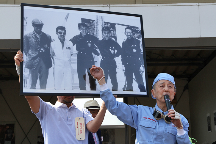 エバーグリーンカップの常勝ドライバーでもある、日本レース界のリビングレジェンドである生沢徹氏。今回は愛機1968年「ポルシェ911T」のエンジントラブルによりレースには不参加だったが、終日レースを見守った。開会式におけるあいさつの際に、数日前に訃報が伝えられた旧友である式場壮吉氏の写真を掲げ、思い出を語った。いわく「（パネル中央の）式場はトヨタ、（その左隣の）石津は三菱、そして（式場の右隣の）自分はプリンスのワークスドライバーだったのに、同じカークラブの仲間ということでおそろいのVANのレーシングスーツを着ていた。そんなことが許された時代だった」とのこと。ちなみに石津とは、VANヂャケットの創業者である石津謙介氏の次男の石津祐介氏である。