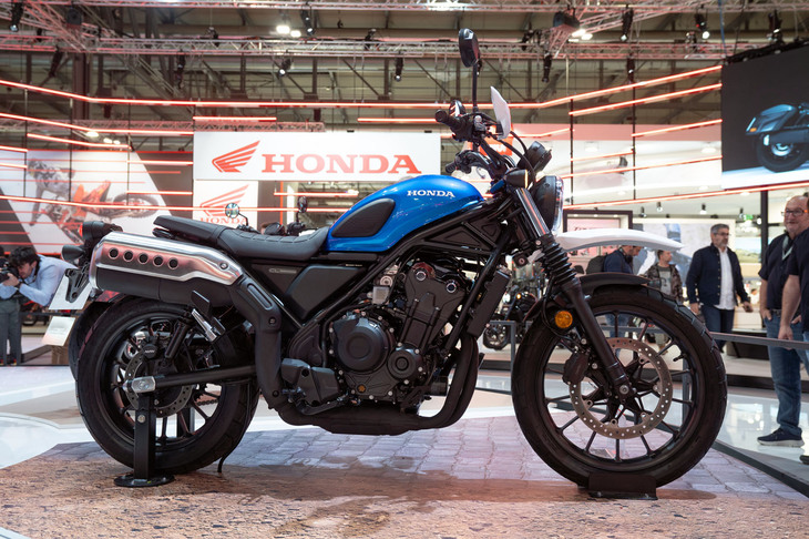 そのウワサを聞いたときはちょっと信じられなかったが、EICMAで発表された「ホンダCL500」は、想像していたよりずっとスクランブラーだった。信じられなかった理由は、このCLがボバースタイルのクルーザーモデル「レブル500」のプラットフォームを使用していることだ。スタンダードなネイキッドモデルをベースに、車高を上げたり下げたりしてバリエーションモデルを構築していくのであれば理解できる。しかし、後ろ下がりのクルーザーモデルをベースに、スッと車高を上げて、オフロードもオンロードも軽やかに駆けるスクランブラーをつくるのは容易ではない。しかし、実車を見る限りそれができていた。前後16インチの極太タイヤを履いたレブルから、フロント19インチ／リア17インチへとホイール系を変更。あわせてサスペンションも“足長”なものとし、車体姿勢をスクランブラー的に仕上げている。加えて、後ろ下がりのフレームラインにあわせた燃料タンクもその形状を変更。トレリスフレームのボトムラインと燃料タンクのボトムライン、そしてシートレールのラインを直線的にデザインすることで、スクランブラーモデルらしい水平基調のデザインがつくり上げられている。写真で見るとポッテリとしたサイレンサーのせいで鈍重に見えるが、実車はスリムで爽やかに仕上げられている。